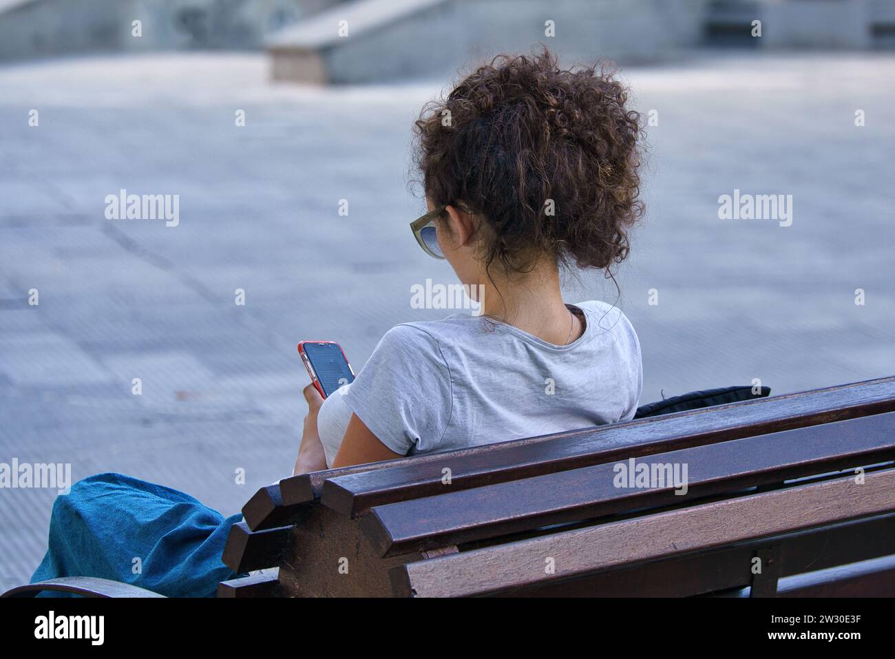Solitude in the Digital Age : une jeune femme trouve son propre espace dans le parc, immergée dans le monde virtuel sur son téléphone Banque D'Images