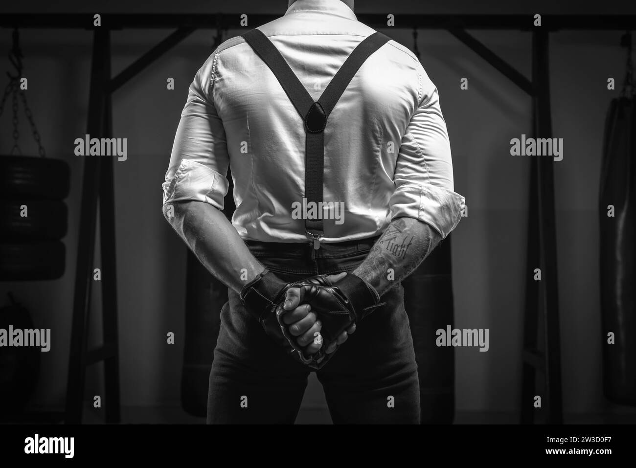 Image d'un homme brutal dans une chemise blanche et bretelles debout dans la salle de gym avec son dos à la caméra. Arts martiaux mixtes Le concept de poing Banque D'Images