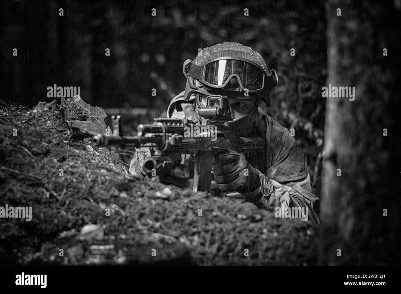 Portrait d'un soldat dans la forêt. Il est assis à l'abri et se prépare à tirer. Concept de protection des frontières. Supports mixtes Banque D'Images