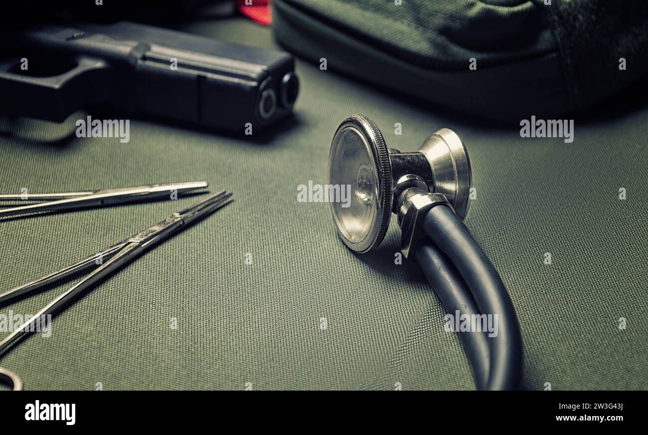 Trousse de premiers soins, phonendoscope, ensemble de ciseaux avec un pistolet reposent sur un fond vert. Vue en haut le concept de médecine militaire. Supports mixtes Banque D'Images