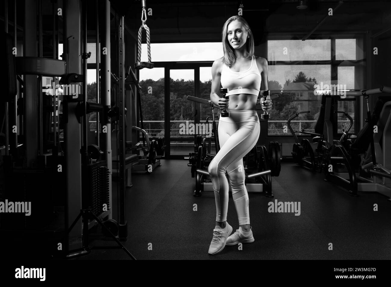 Charmante jeune sportswoman posant dans la salle de gym. Concept de culturisme. Sport. Haltérophilie. Supports mixtes Banque D'Images