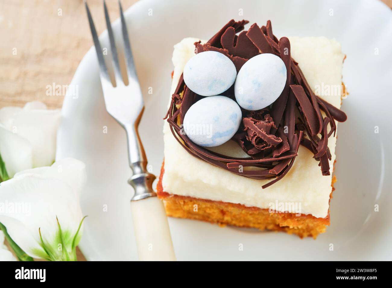 Barres de gâteau aux carottes de Pâques décorées avec nid de chocolat et œufs de bonbons au chocolat fleurissant des fleurs de cerise ou de pomme sur des fonds rustiques en bois clair. Banque D'Images