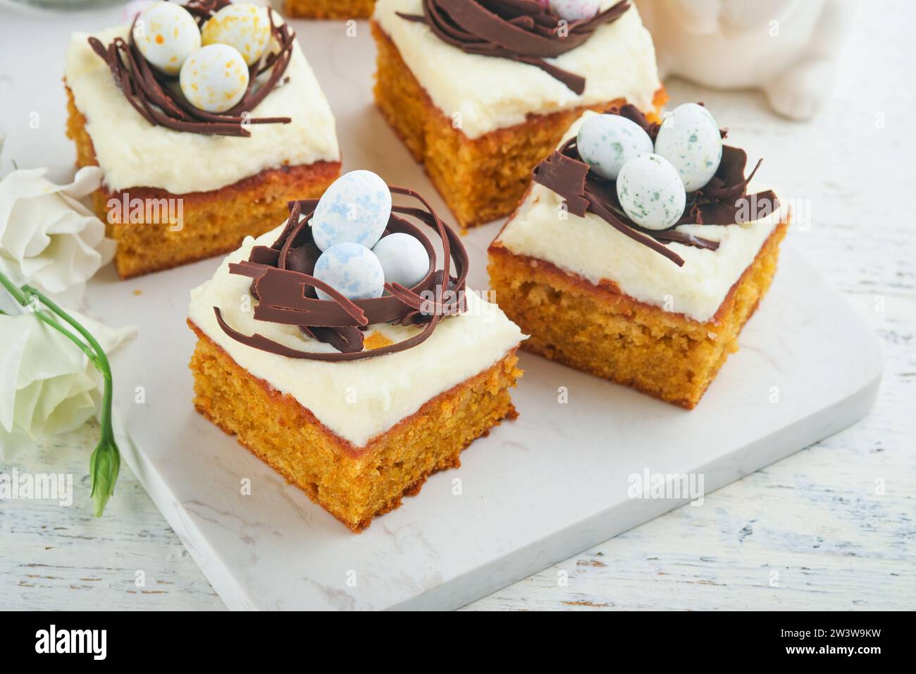 Barres de gâteau aux carottes de Pâques décorées avec nid de chocolat et œufs de bonbons au chocolat fleurissant des fleurs de cerise ou de pomme sur des fonds rustiques en bois clair. Banque D'Images