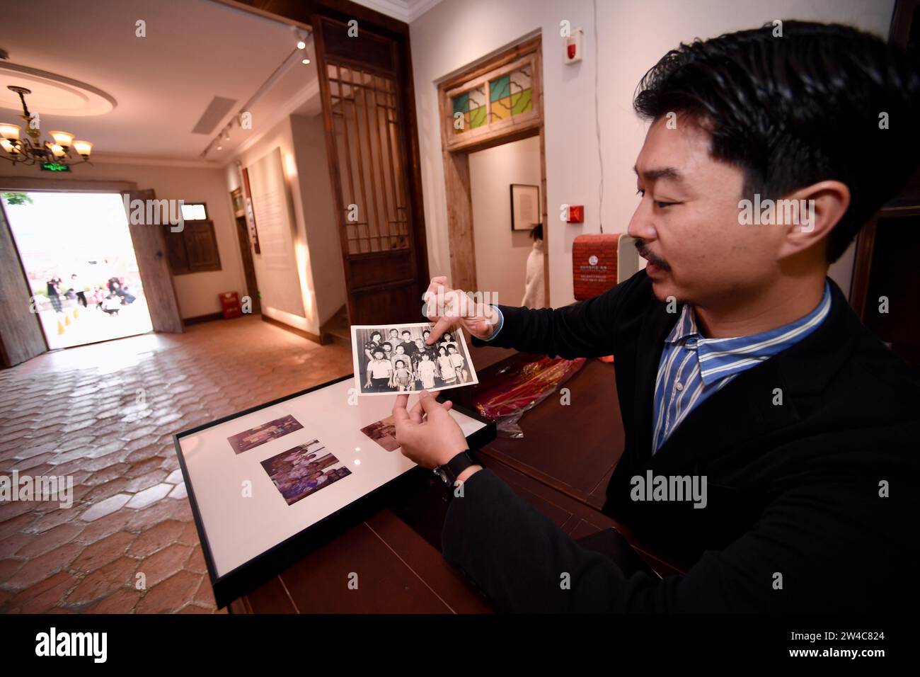JINJIANG, 21 décembre 2023 (Xinhua) -- Wu Shaopeng, conservateur d'art et descendant de Chinois d'outre-mer, montre de vieilles photos de famille renvoyées des Philippines dans le village de Wulin de Jinjiang, dans la province du Fujian, dans le sud-est de la Chine, le 19 décembre 2023. Dans le village de Wulin, dans la province du Fujian de l'est de la Chine, les visiteurs sont souvent fascinés par le mélange de styles architecturaux : maisons locales en briques rouges, bâtiments gothiques, structures gréco-romanes et bâtiments mêlant éléments chinois et occidentaux. Le mélange éclectique de styles architecturaux raconte de façon vivante l'histoire de la connexion du village avec Banque D'Images