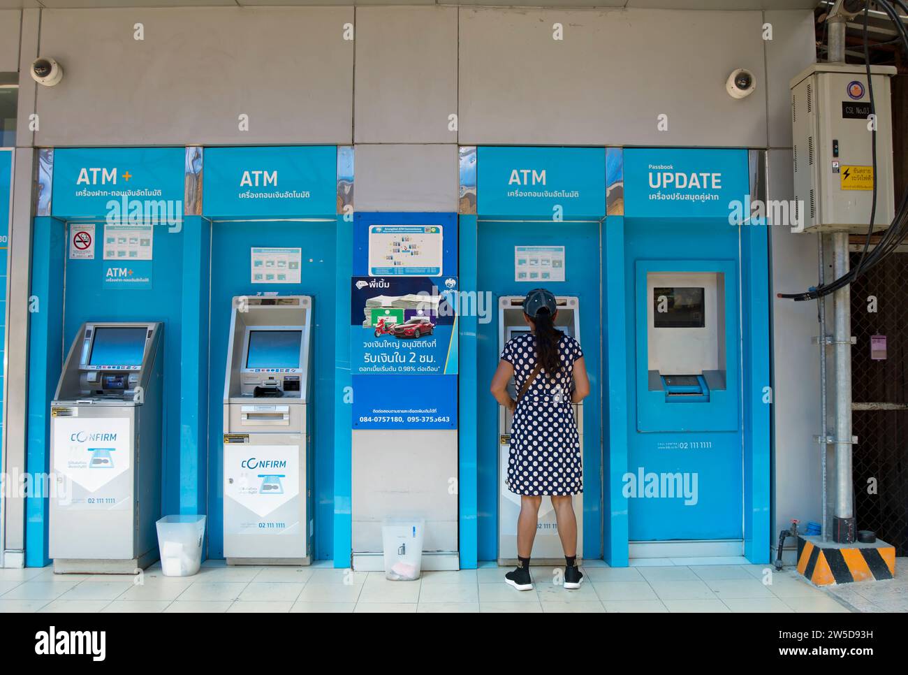 une femme portant une robe à pois et une casquette de baseball utilise un distributeur automatique de billets à phetchabun, en thaïlande Banque D'Images