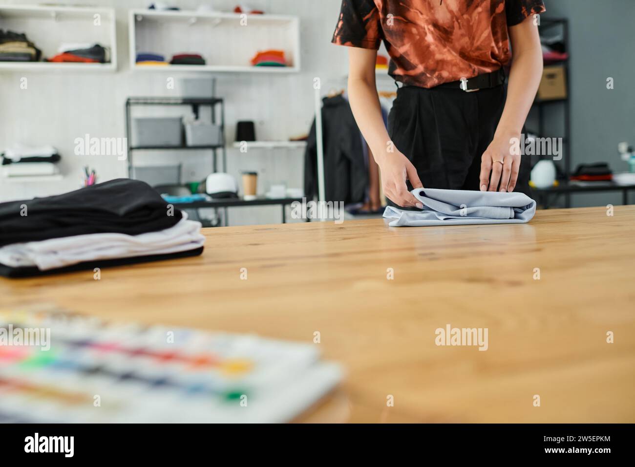 vue partielle de femme expérimentée pliant des vêtements sur la table dans l'atelier d'impression textile, petite entreprise Banque D'Images