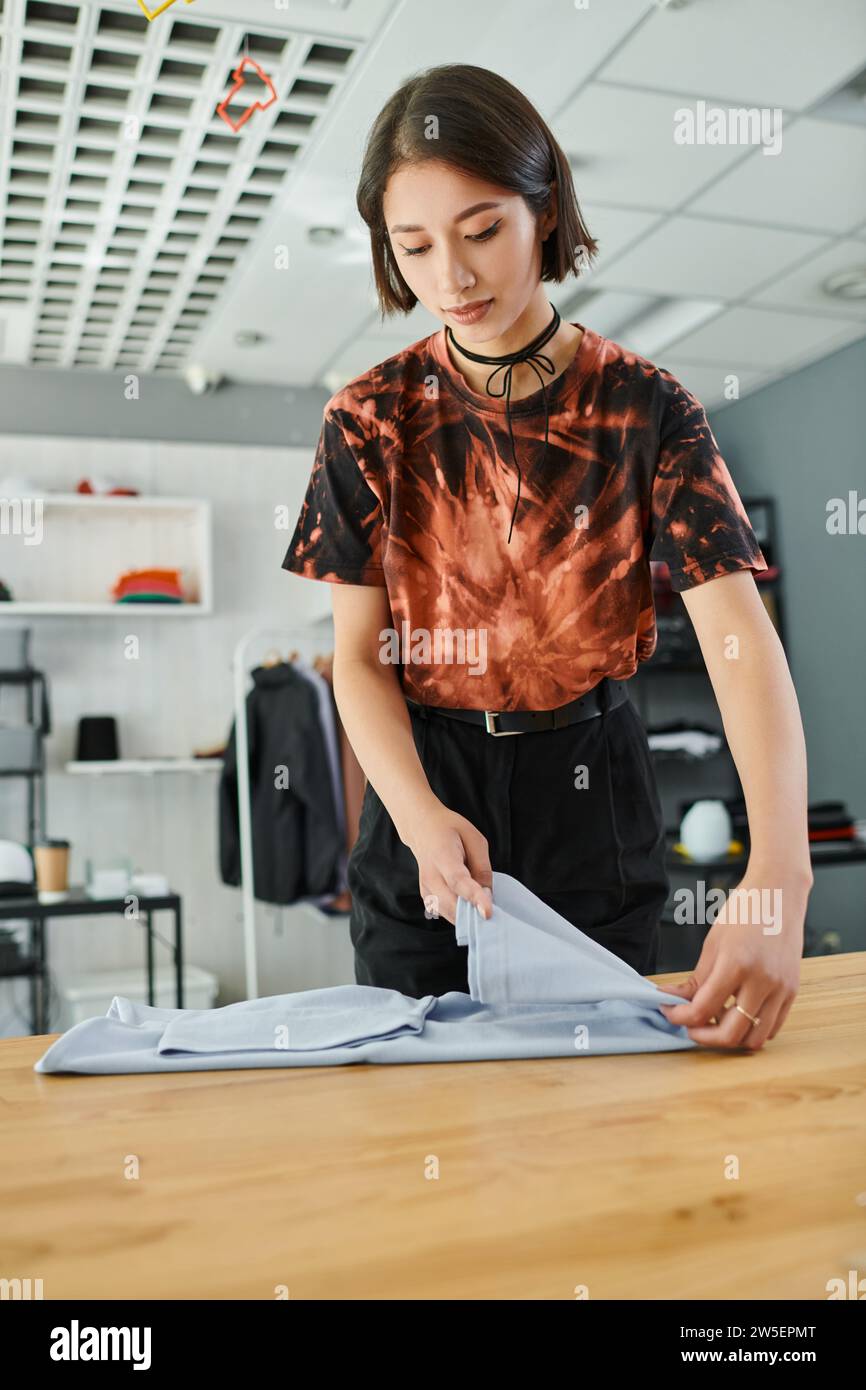 jeune et tendance femme asiatique pliant des vêtements sur la table dans le studio d'impression textile, petite entreprise Banque D'Images