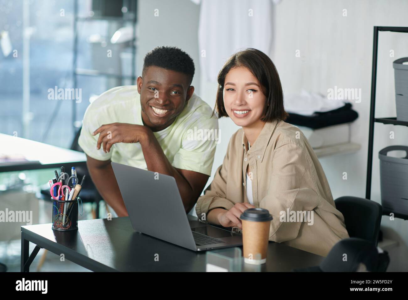 joyeux entrepreneurs multiethniques regardant la caméra dans le studio d'impression de vêtements, petite entreprise Banque D'Images