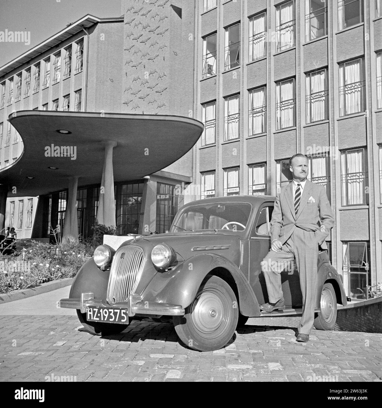 M. de visser debout devant son Simca 8 devant le bâtiment principal de KLM à la Haye ca. Août 1951 Banque D'Images
