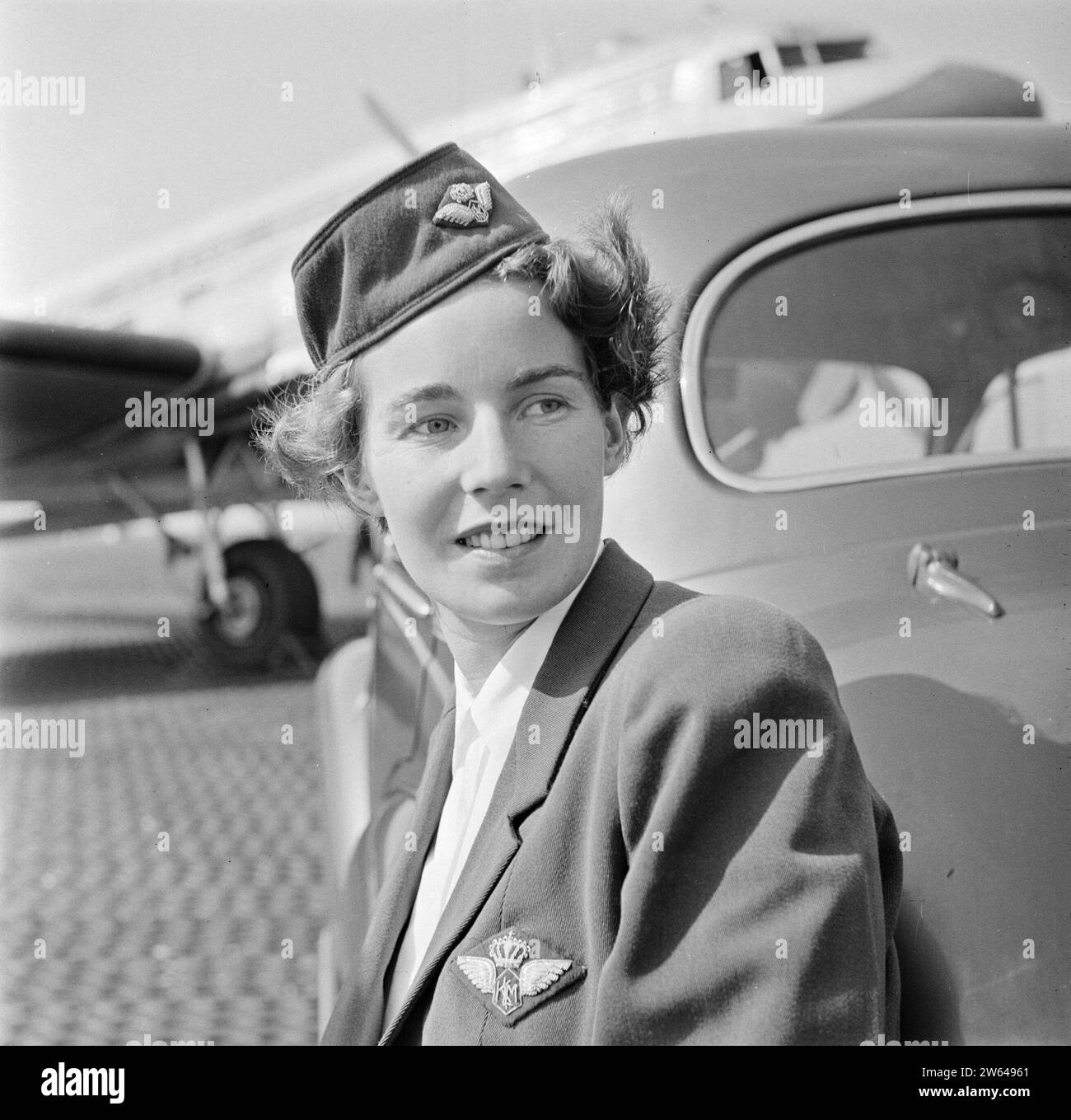 Portrait d'un agent de bord KLM appuyé contre une voiture avec un Douglas DC-3 en arrière-plan ca. Août 1951 Banque D'Images