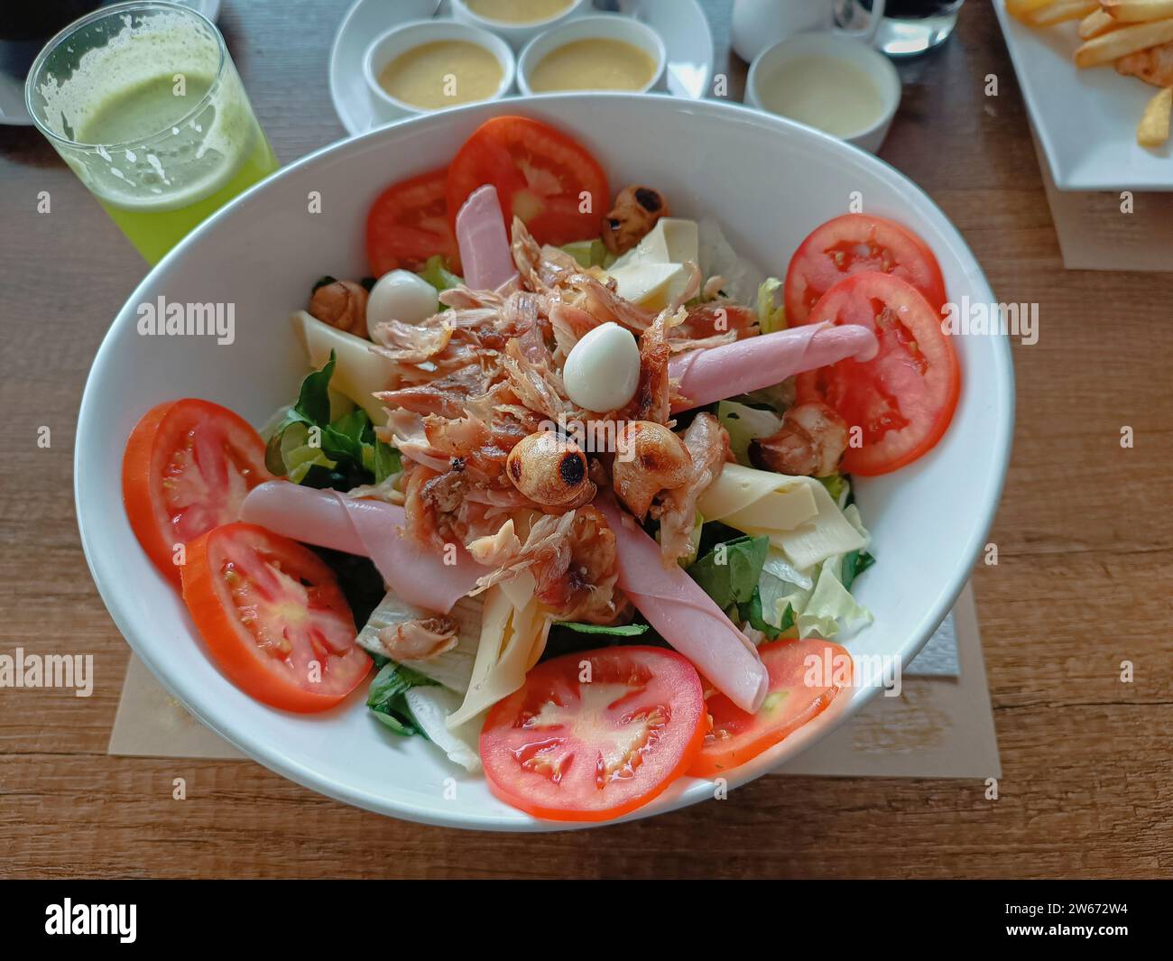Salade fraîche décorée de poulet grillé, jambon, fromage, champignons et œufs de caille sur une assiette blanche profonde Banque D'Images