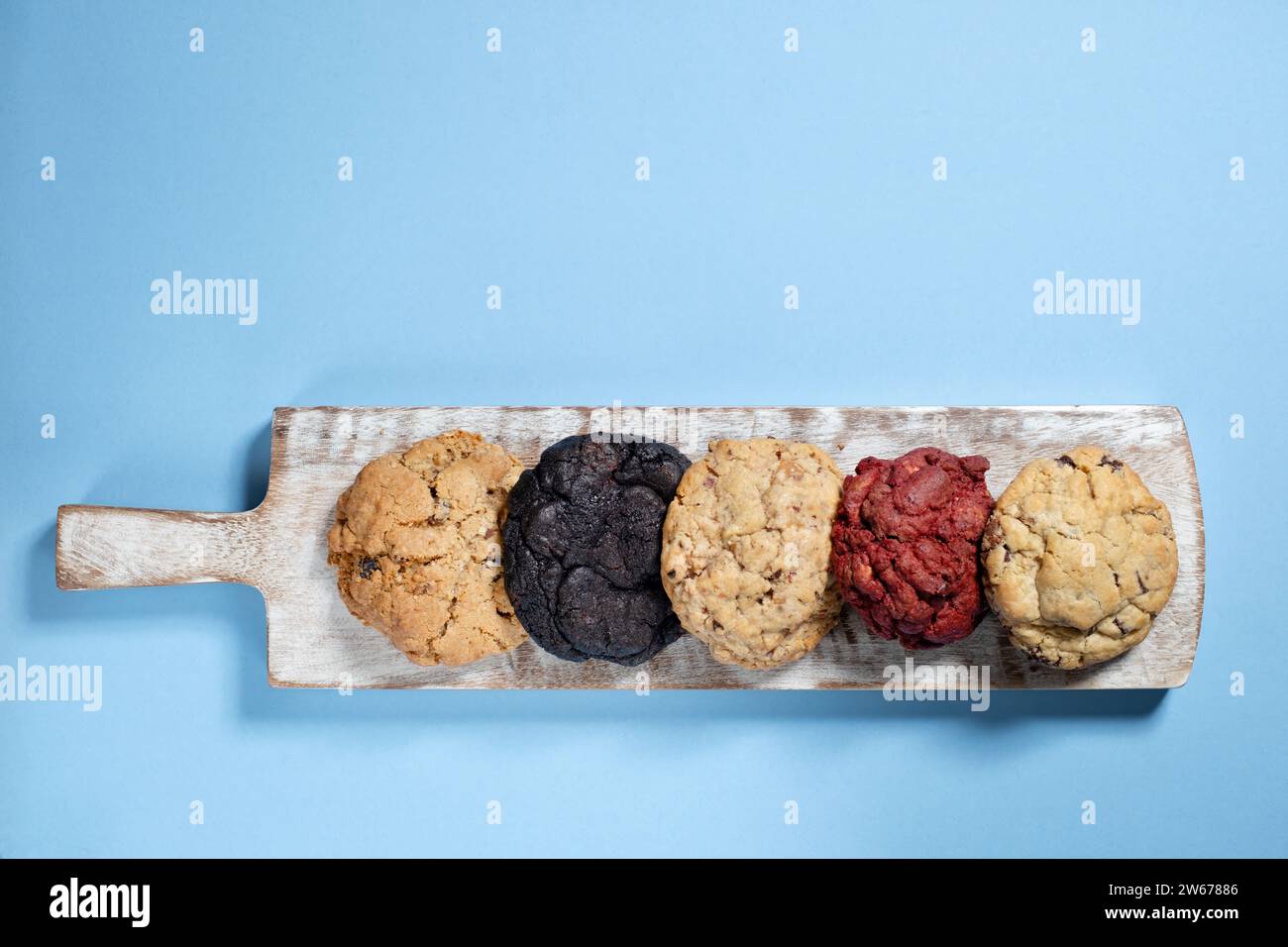 Une sélection de cookies de style NY fraîchement préparés alignés sur un plateau de service et photographiés sur un fond Uni Banque D'Images Une sélection de cookies de style NY fraîchement préparés alignés sur un plateau de service et photographiés sur un fond Uni Banque D'Images