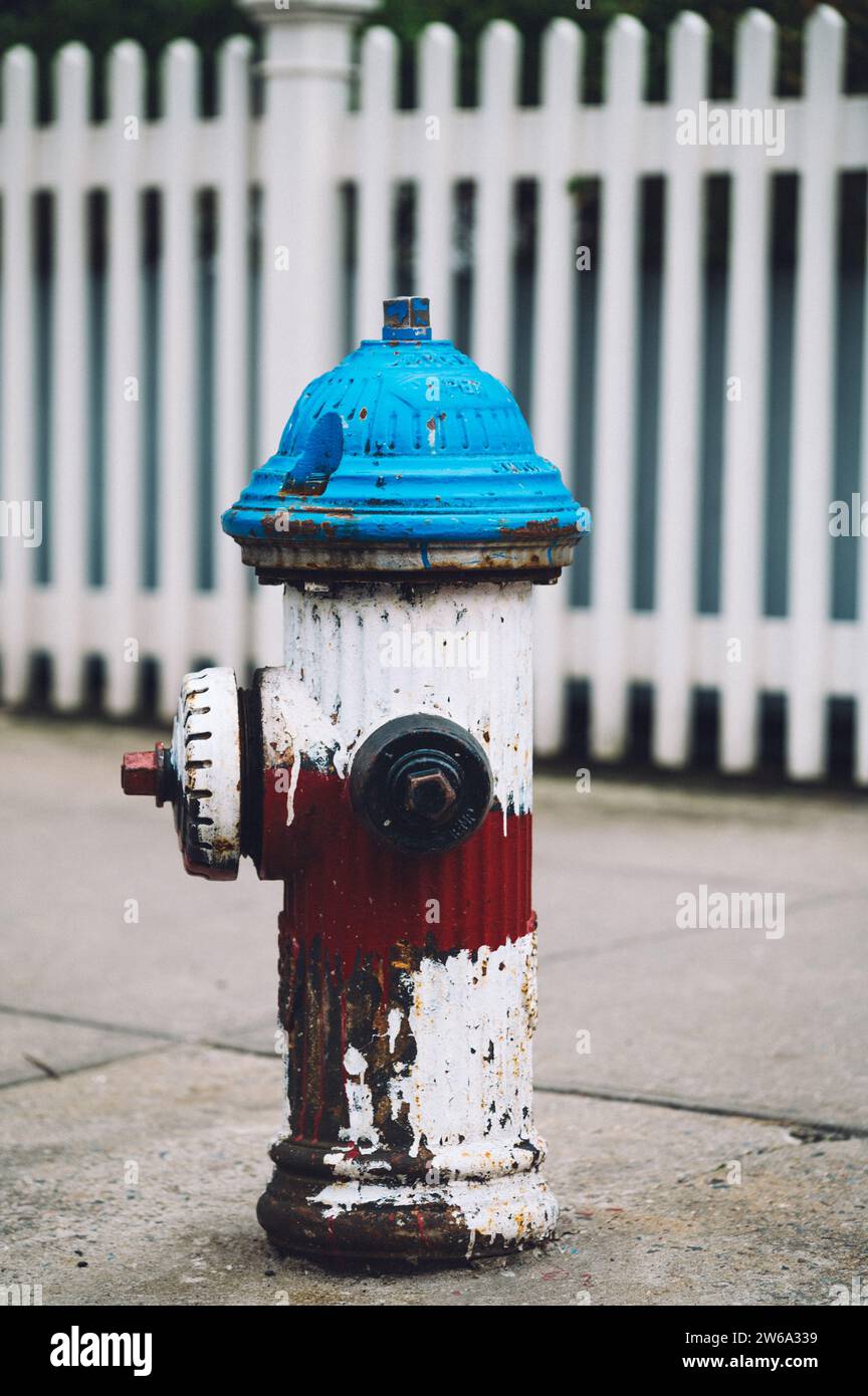 Une bouche d'incendie bleue et rouge vintage se dresse bien en vue sur une clôture de piquet blanche en toile de fond à Manhattan, New York.titre : bouche d'incendie vintage dans Man Banque D'Images