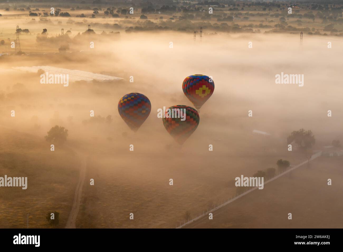 D'en haut plusieurs montgolfières colorées s'élèvent au-dessus d'un paysage englouti par le brouillard avec le soleil projetant une douce lueur sur la scène Banque D'Images