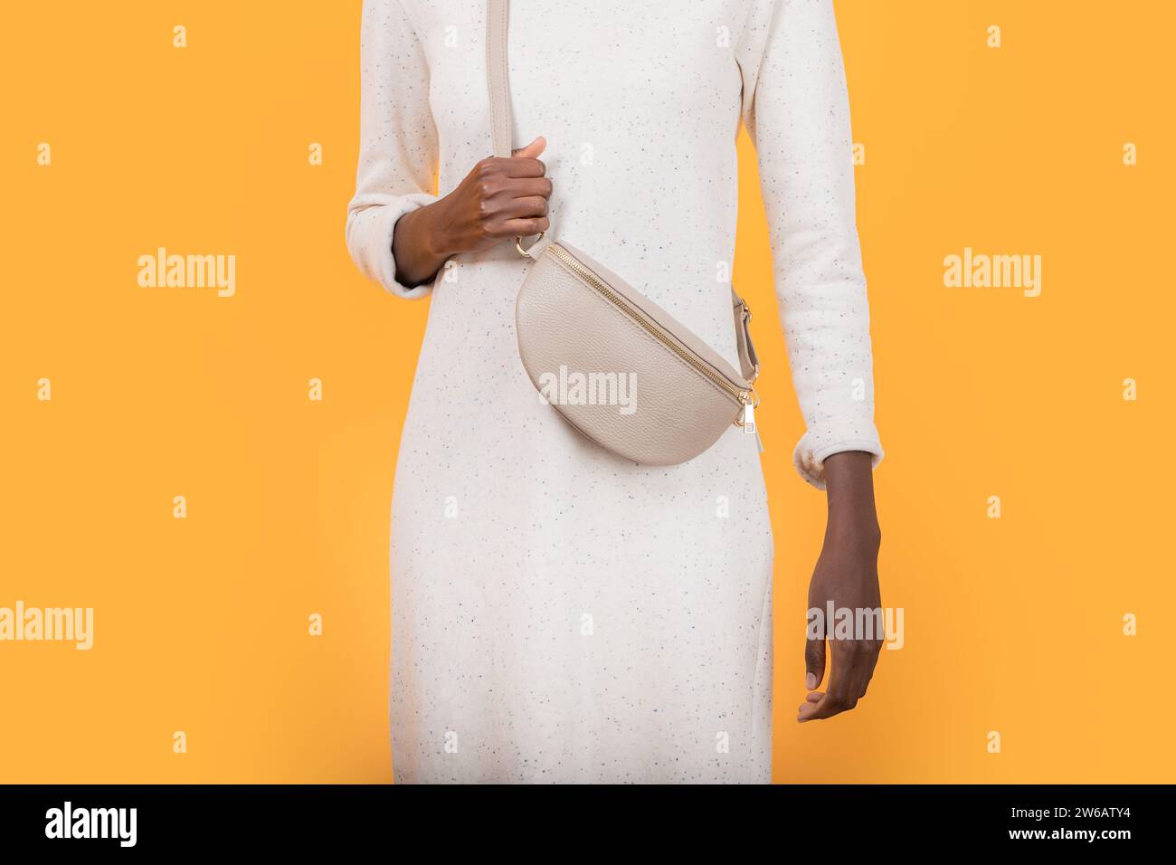 Crop anonyme mince femme afro-américaine en robe blanche avec porter sac à bandoulière tendance tout en se tenant sur fond jaune Banque D'Images