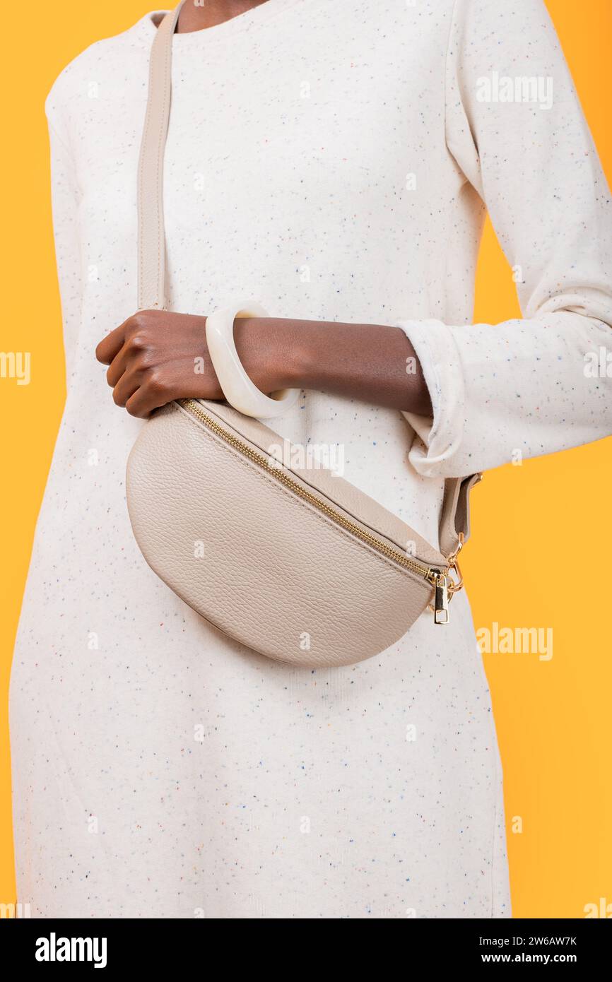 Crop anonyme mince femme afro-américaine en robe blanche avec porter sac à bandoulière tendance tout en se tenant sur fond jaune Banque D'Images