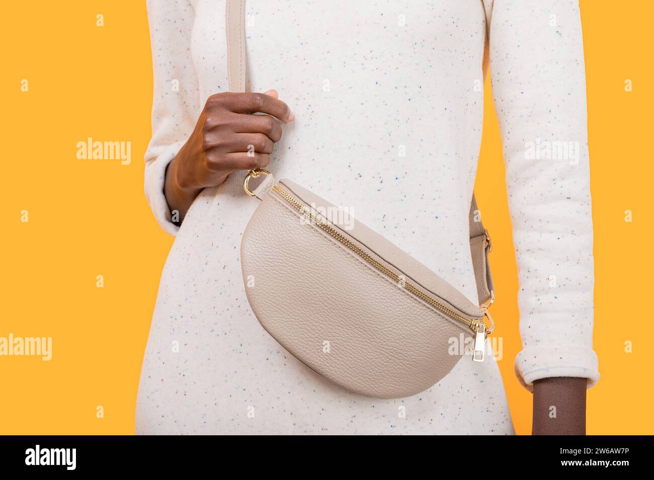 Crop anonyme mince femme afro-américaine en robe blanche avec porter sac à bandoulière tendance tout en se tenant sur fond jaune Banque D'Images