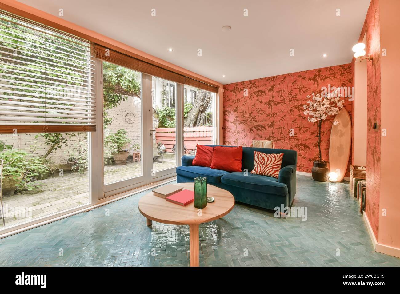 Papier peint rose avec plancher bleu dans le salon avec canapé et table basse par une grande porte vitrée à l'appartement moderne Banque D'Images