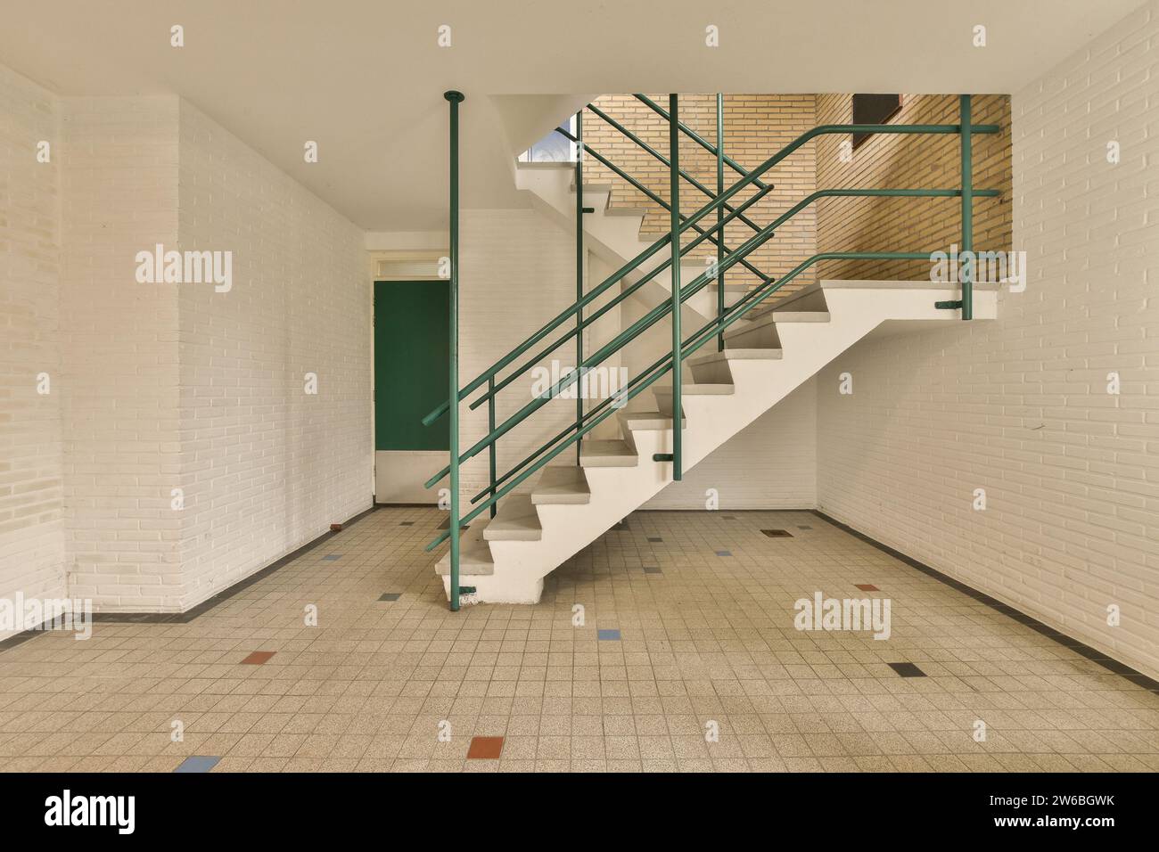 Immeuble de bureaux avec escalier vide et main courante verte menant au deuxième étage entouré de murs blancs et sol carrelé Banque D'Images