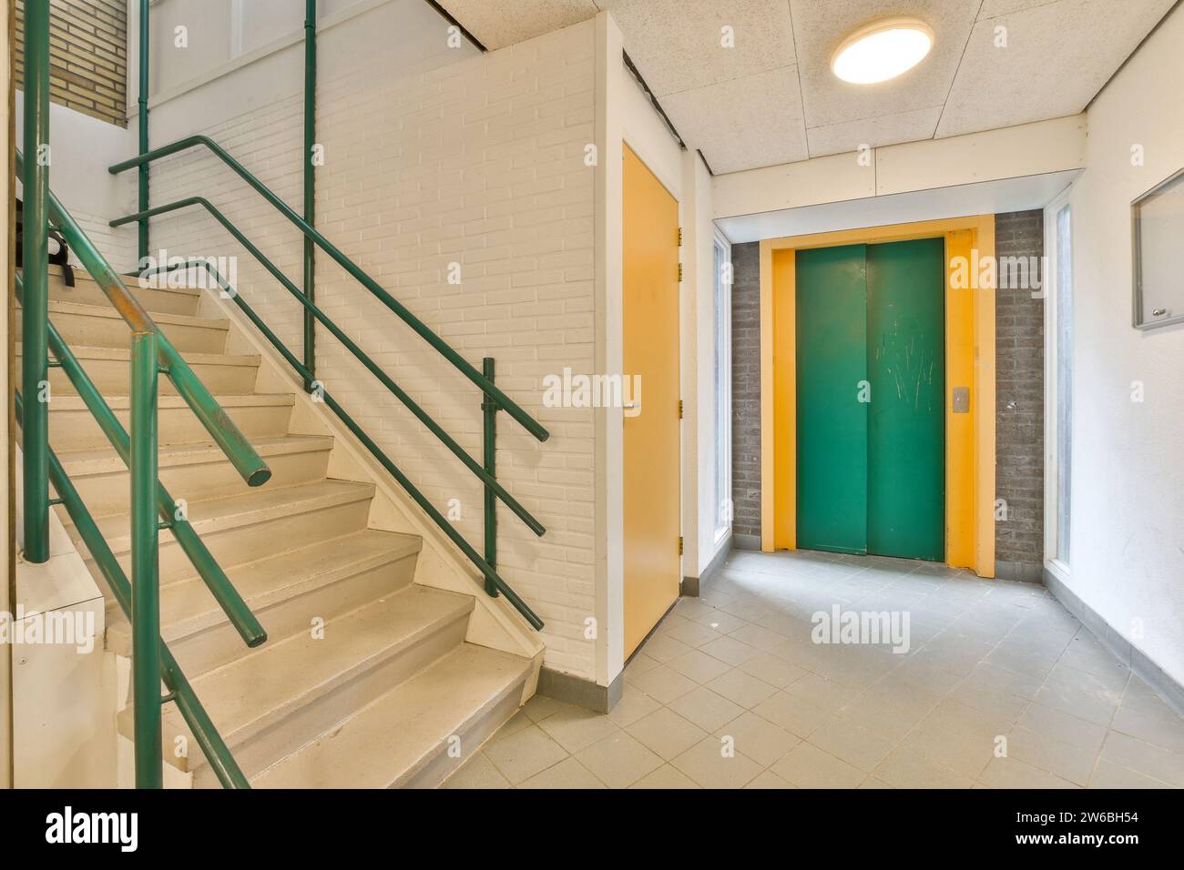 Intérieur de l'immeuble de bureaux moderne avec escalier vide et couloir menant à l'ascenseur vert et carrelage blanc Banque D'Images