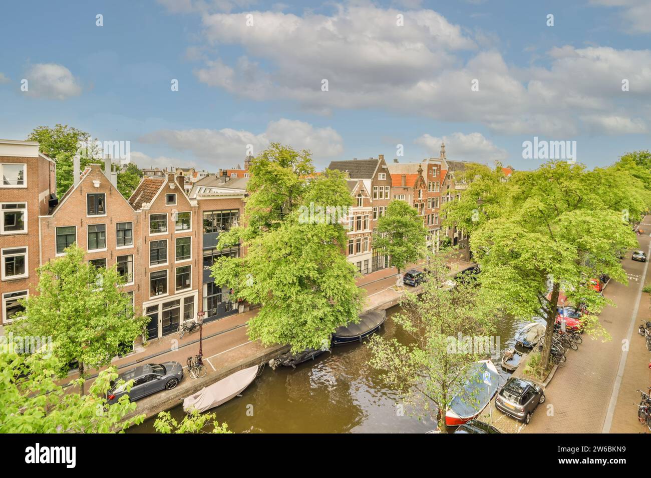 Vue panoramique sur le canal d'Amsterdam entouré d'arbres verdoyants et de bâtiments hollandais historiques sous un ciel bleu. Banque D'Images
