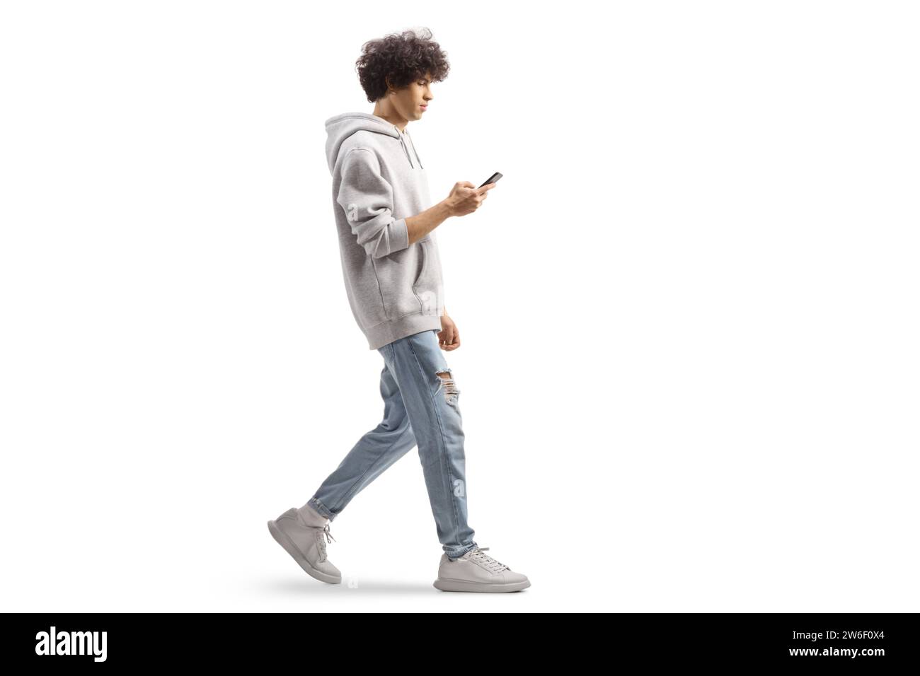 Photo de profil pleine longueur d'un gars de gen z portant un sweat à capuche gris et marchant avec un smartphone isolé sur fond blanc Banque D'Images