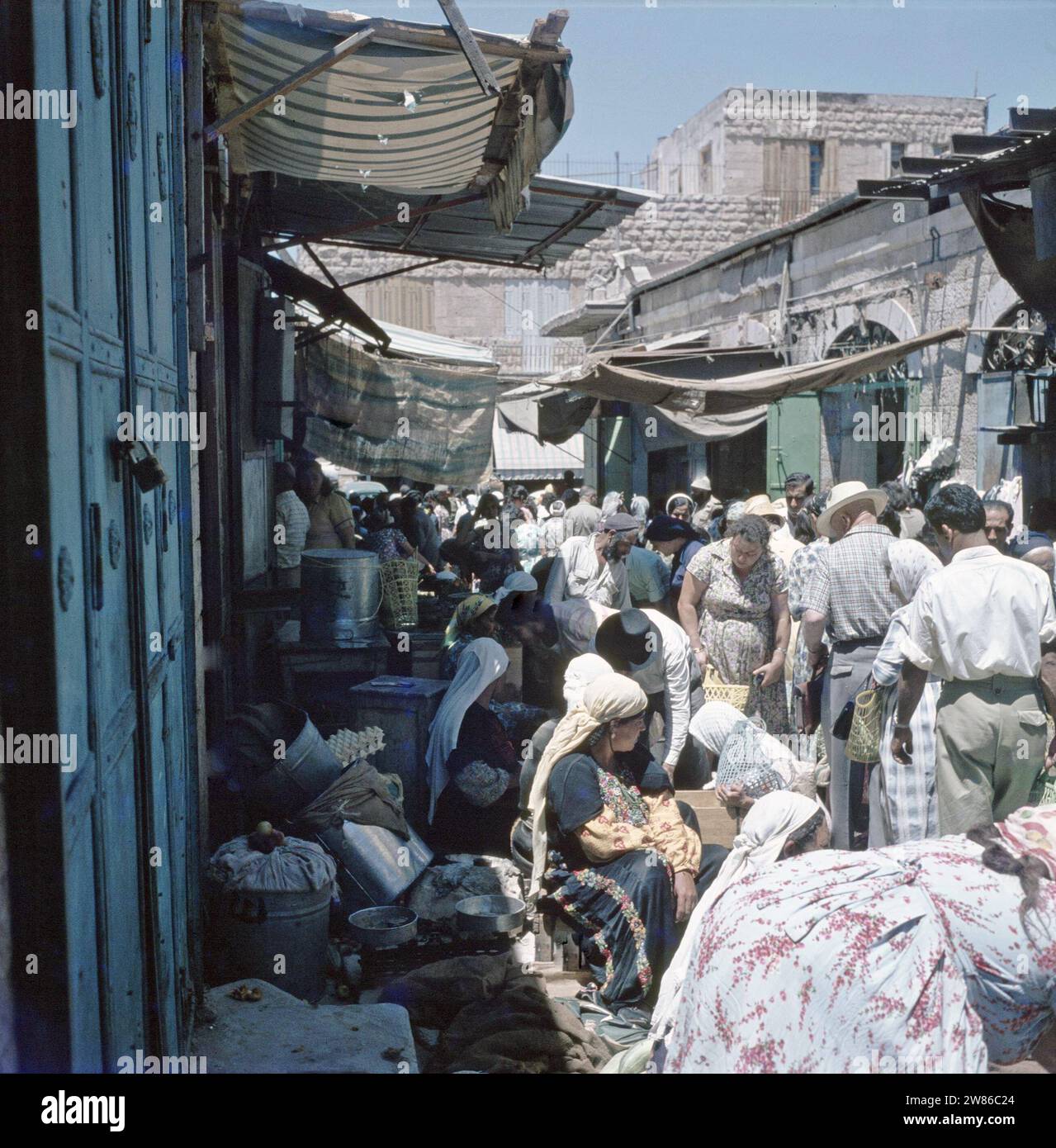 Jérusalem. Scène de marché : dans une rue étroite avec des magasins des deux côtés, les commerçants ont également exposé leurs marchandises au milieu de la route, au premier plan à gauche une femme en costume traditionnel avec une échelle ca. années 1960 Banque D'Images