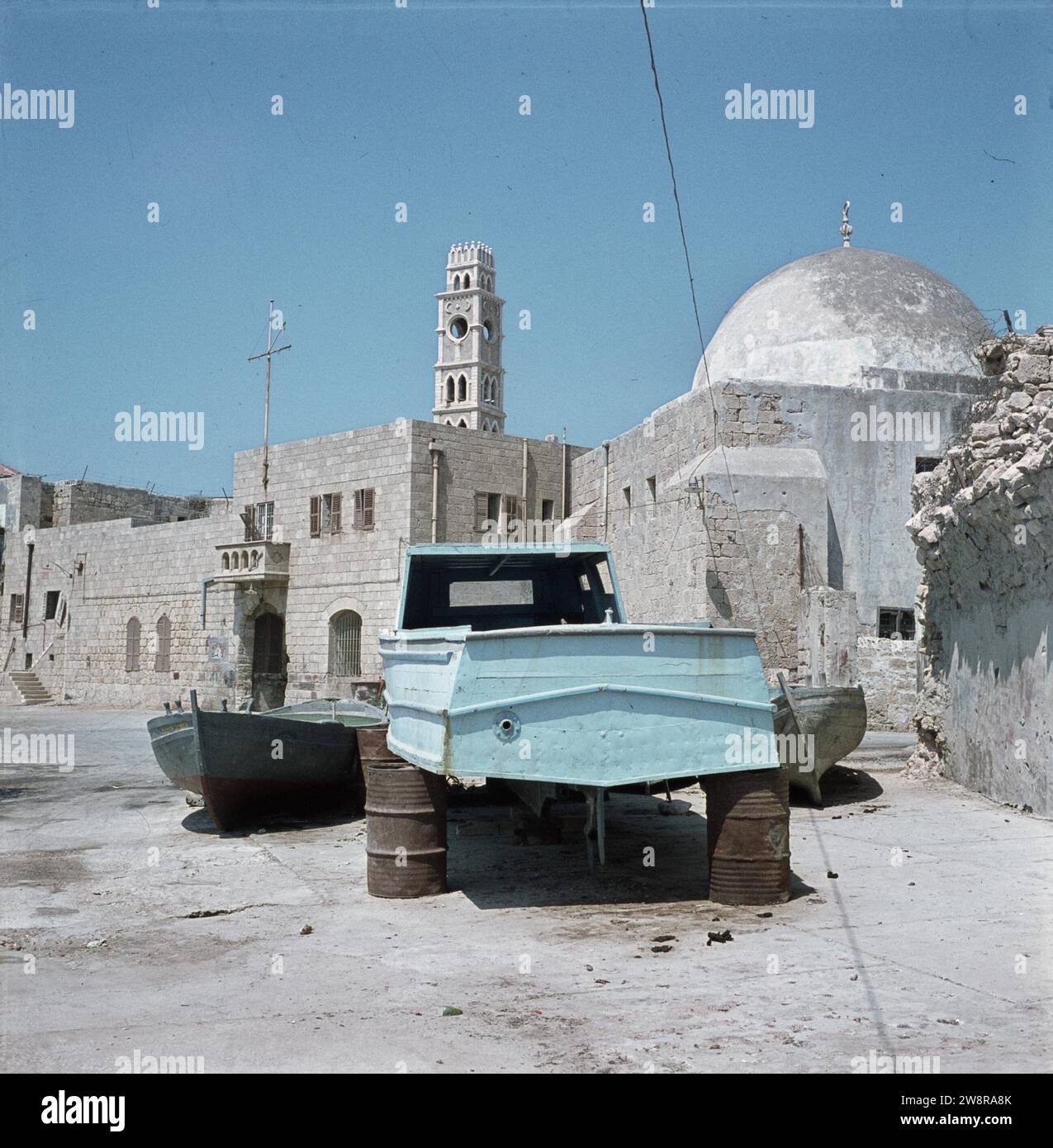 Acre (acre). Front de port avec une perceuse sur des barils d'essence rouillés sur le quai et au-dessus des maisons la tour du caravansérail-avec-les-colonnes et sur la droite un dôme d'une mosquée ca. 1964 Banque D'Images