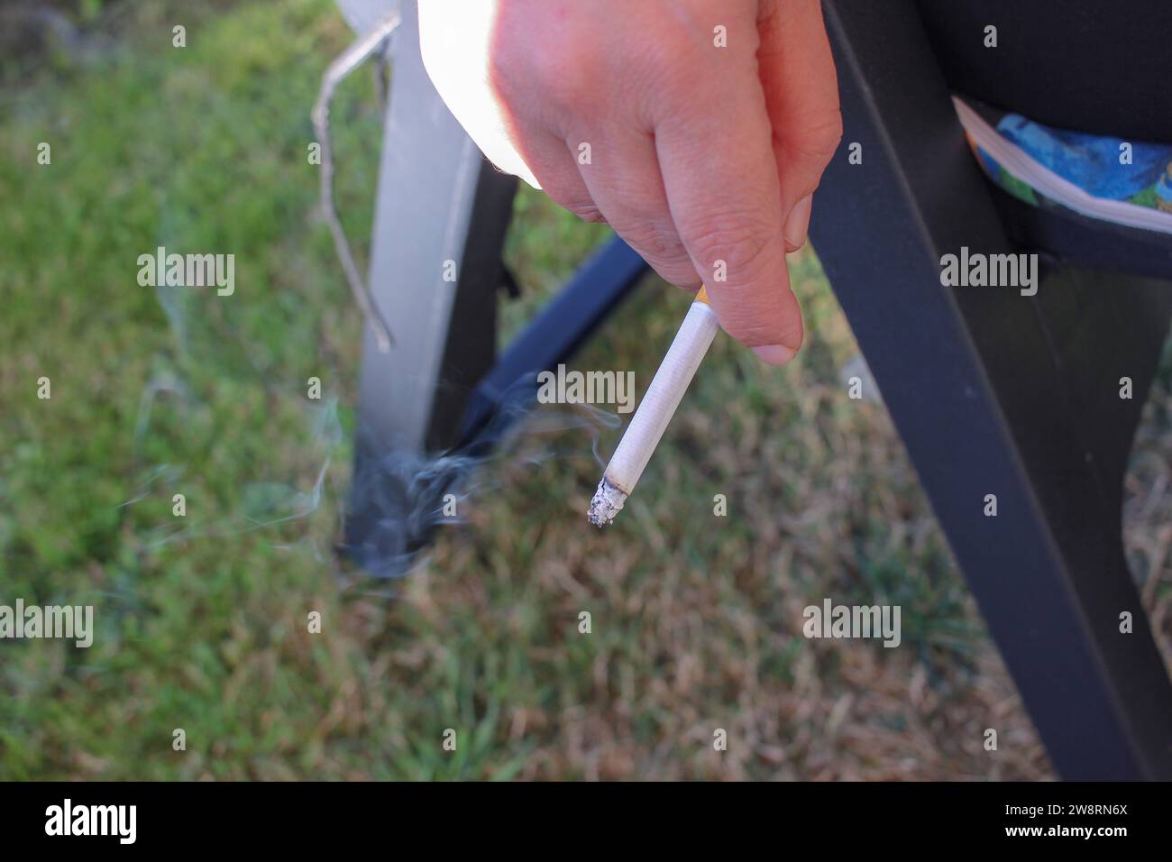 Contrastes dans la nature : main de femme avec cigarette allumée dans le jardin Banque D'Images