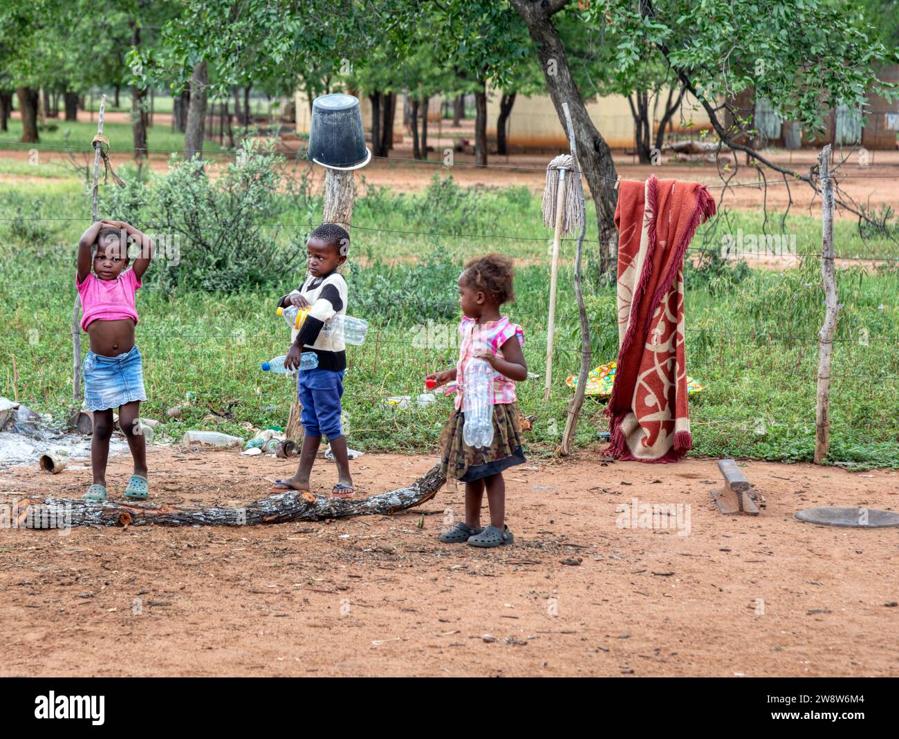 des enfants africains dans le village ramassant des bouteilles en plastique sur un chemin de terre Banque D'Images
