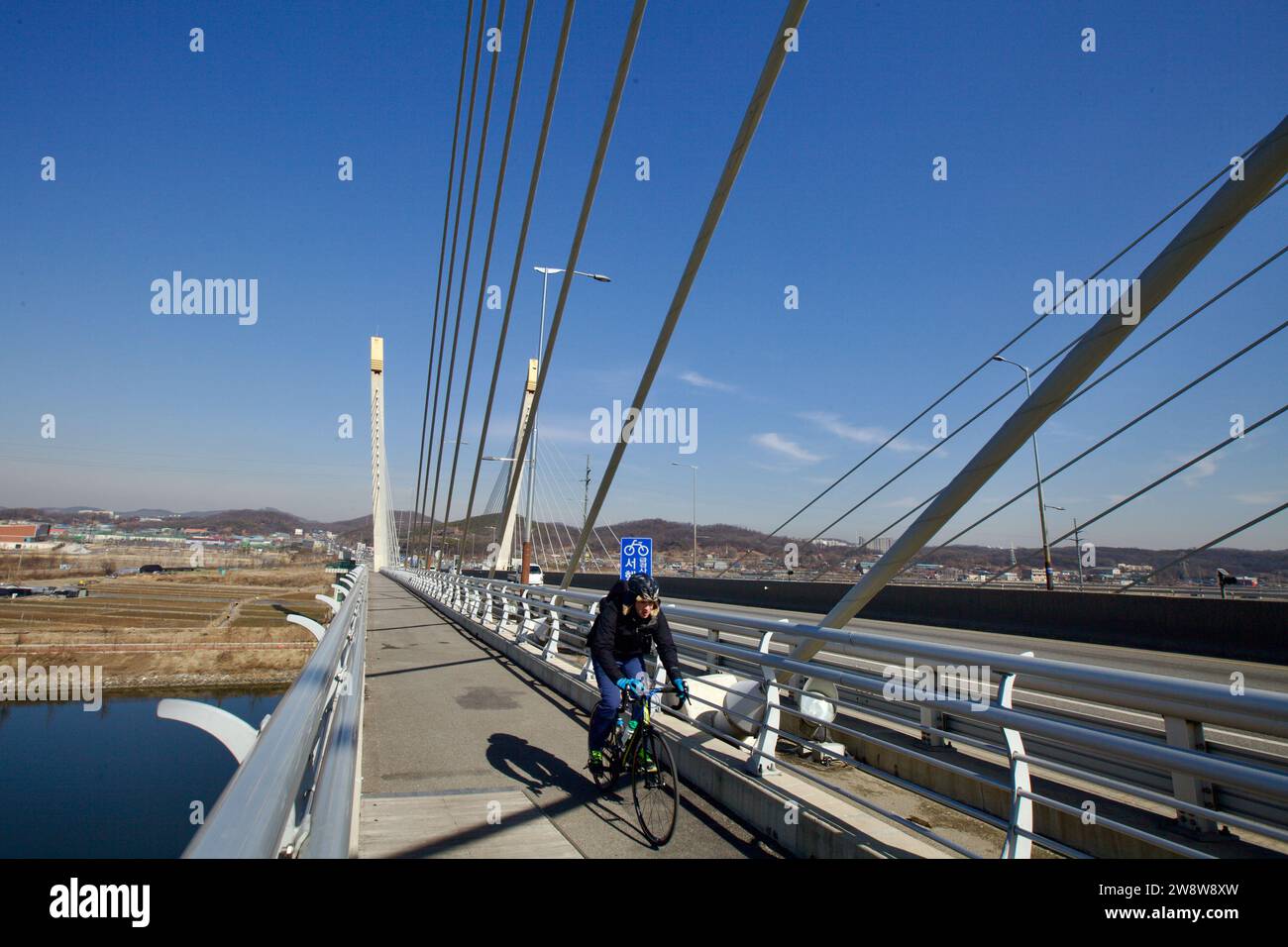 Incheon, Corée du Sud - 10 février 2020 : les cyclistes traversent le pont de Baekseok, ses câbles créant un motif frappant au-dessus de la sereine Gyeongin Ara Banque D'Images
