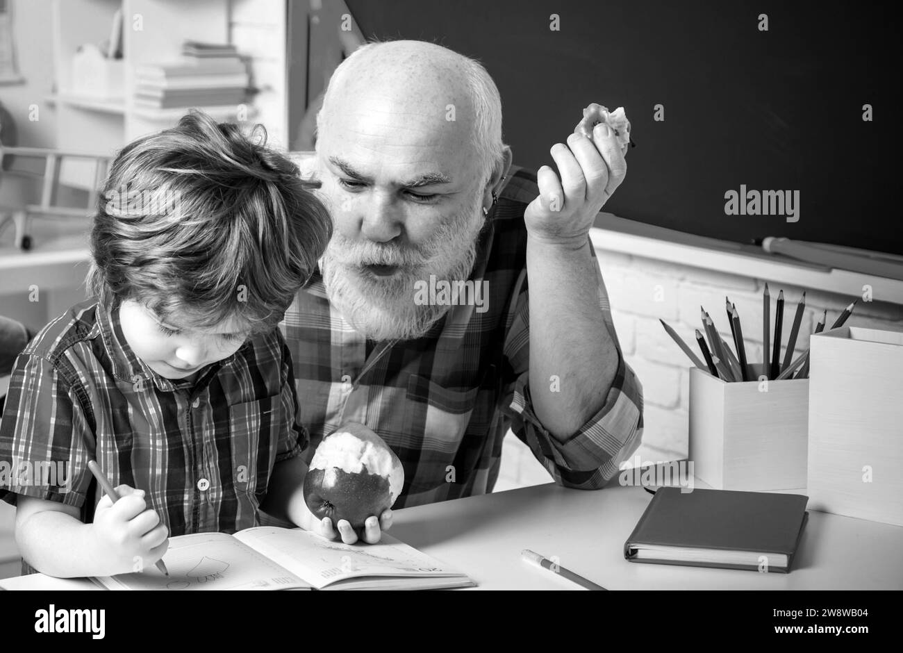 Le grand-père et le petit petit petit-fils adorables étudient et apprennent ensemble. Le grand-père et le petit-fils apprennent à écrire et à lire à l'école. Senior Banque D'Images