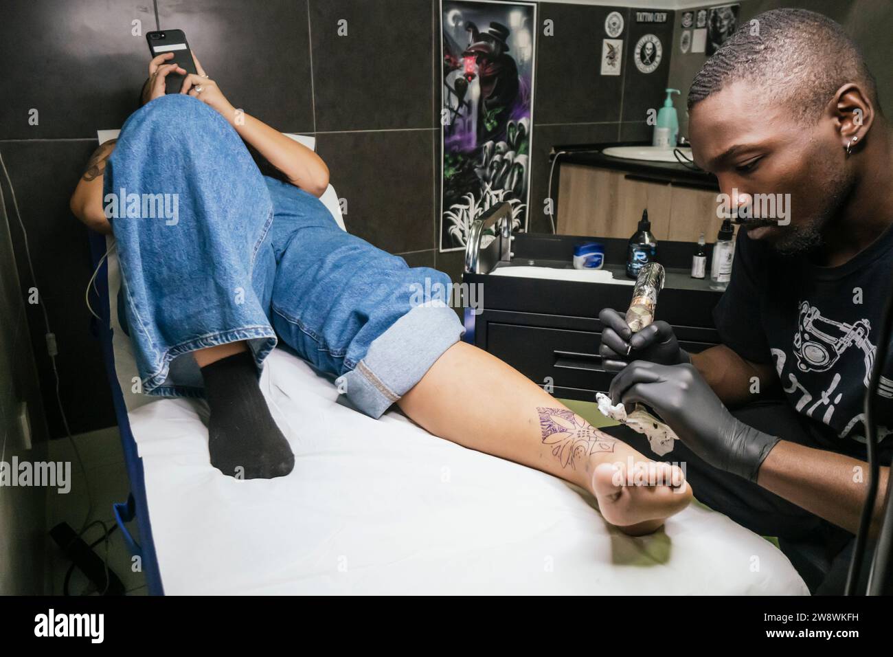 tatoueur noir faisant tatouage sur le pied de son client Banque D'Images