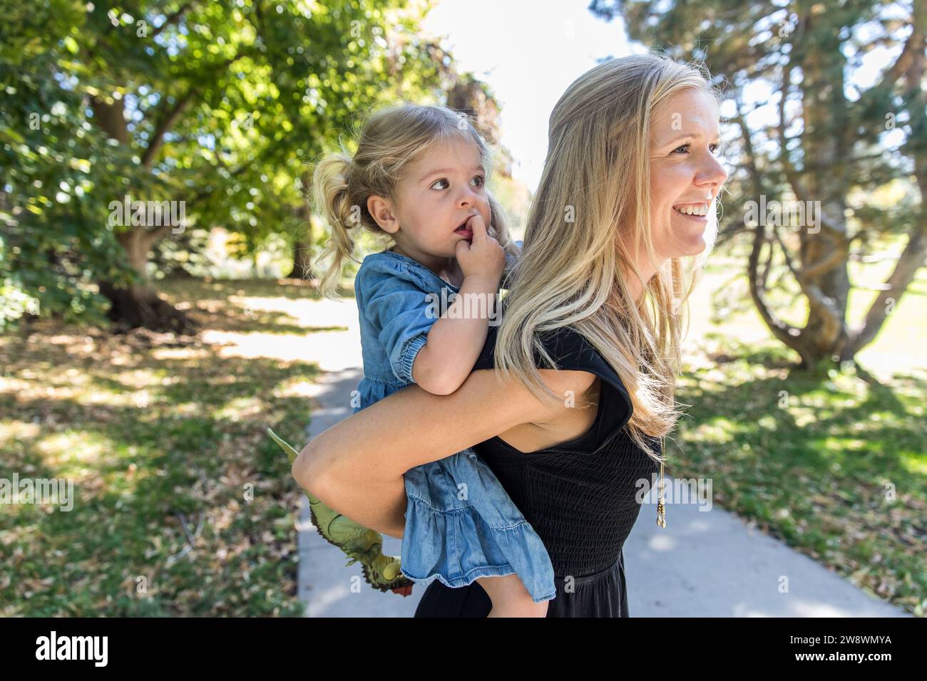 Maman souriant donnant fille cochon sur le trottoir au parc Banque D'Images