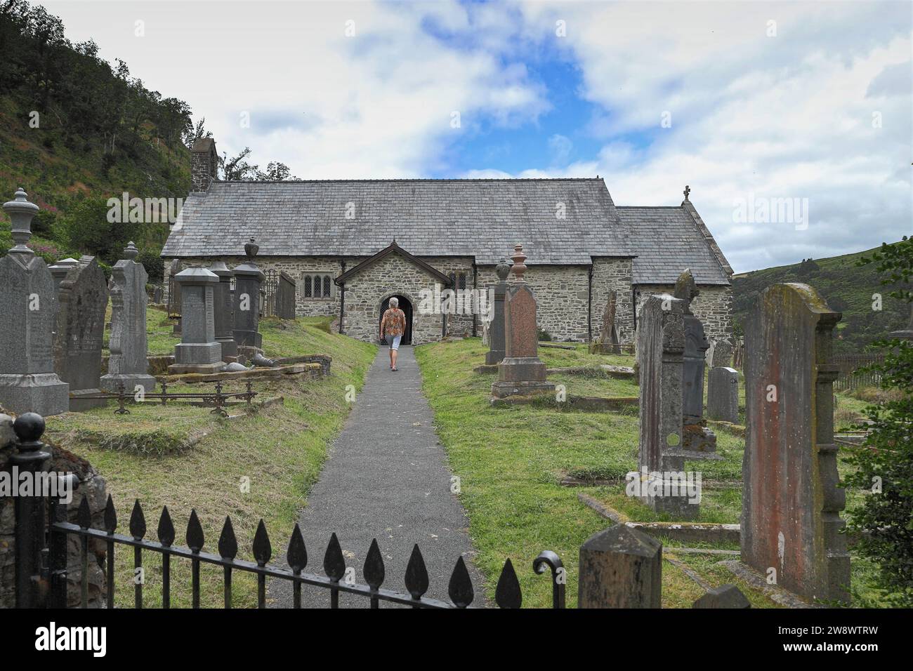 Femme marchant à travers le cimetière vers le porche d'entrée de St Davids Old Church, Llanwrtyd Wells, Powys, pays de Galles, Royaume-Uni Banque D'Images