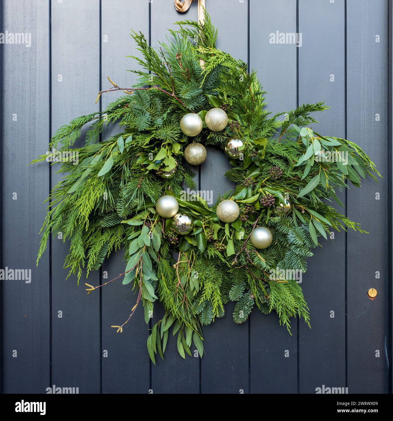 Une modeste couronne de Noël faite de brins de sapin, thuja, eucalyptus et boules d'argent sur une porte gris foncé à Londres. Cadre carré. Banque D'Images