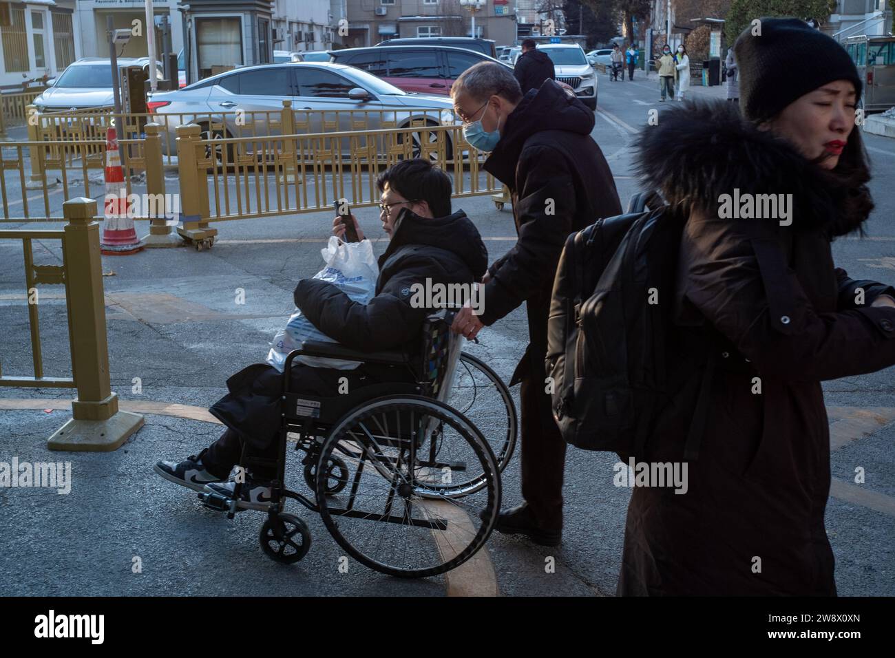 Père chinois pousse son fils malade en fauteuil roulant en quittant un hôpital à Pékin, en Chine. 22-Dec-2023 Banque D'Images