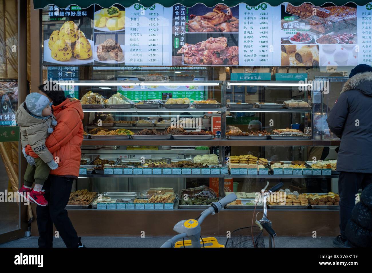 Une femme, avec son enfant dans les bras, quitte un magasin d'alimentation sans dépenser à Pékin, en Chine. 22-Dec-2023 Banque D'Images