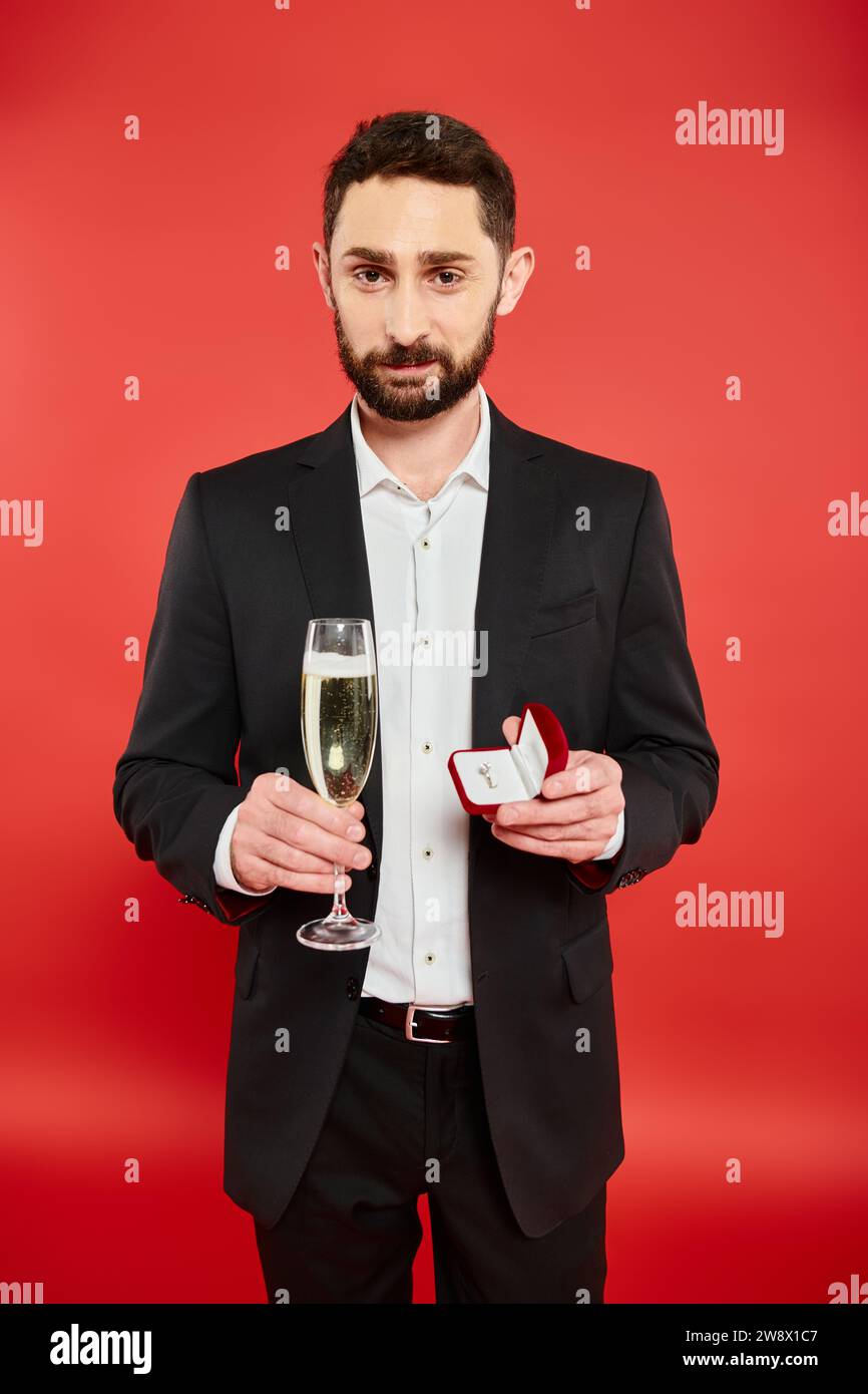 Homme barbu souriant en tenue élégante avec champagne et boîte à bijoux le jour de la Saint Valentin Banque D'Images
