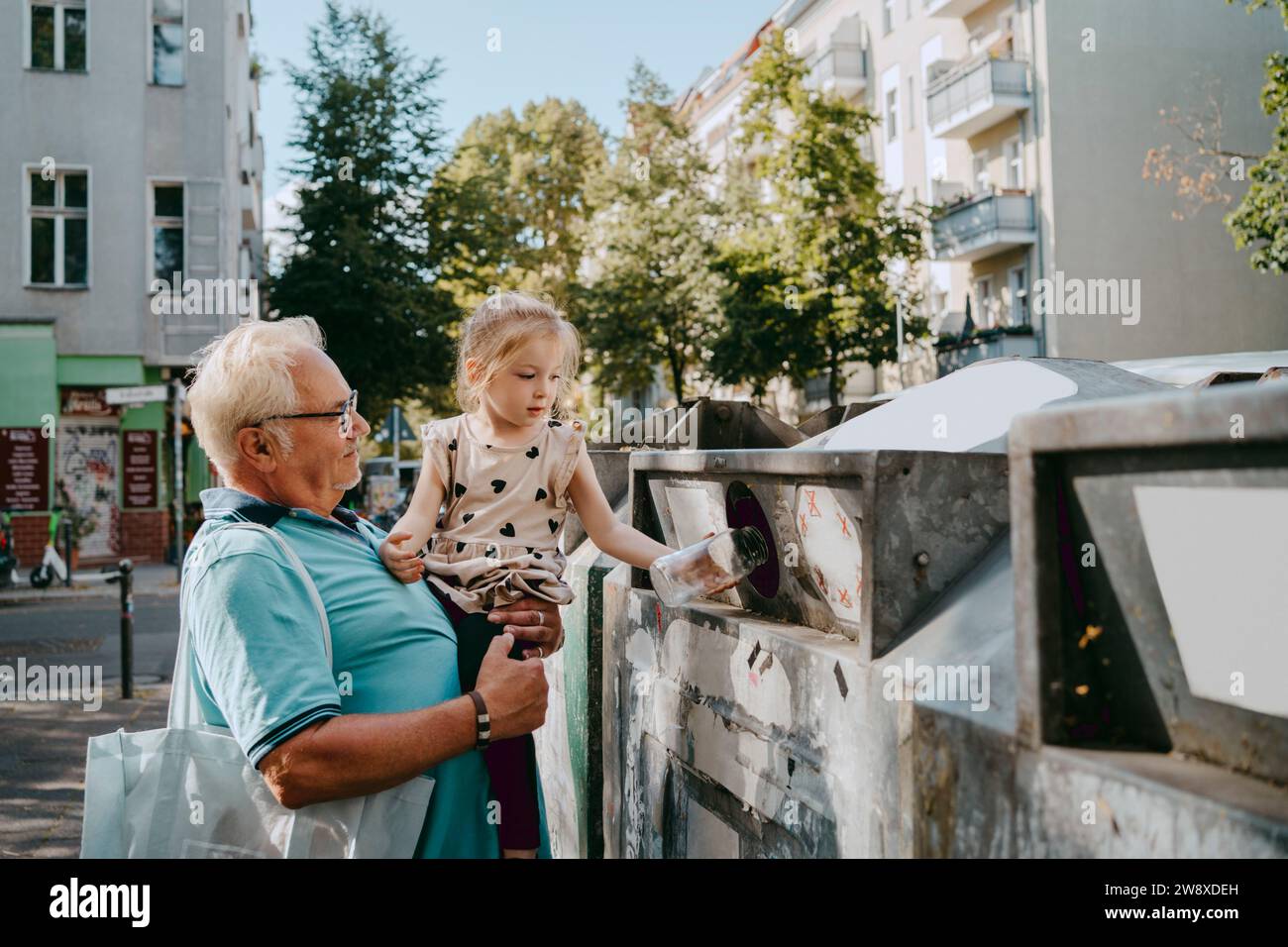 Homme âgé portant sa petite-fille jetant des ordures dans une boîte dans la rue Banque D'Images