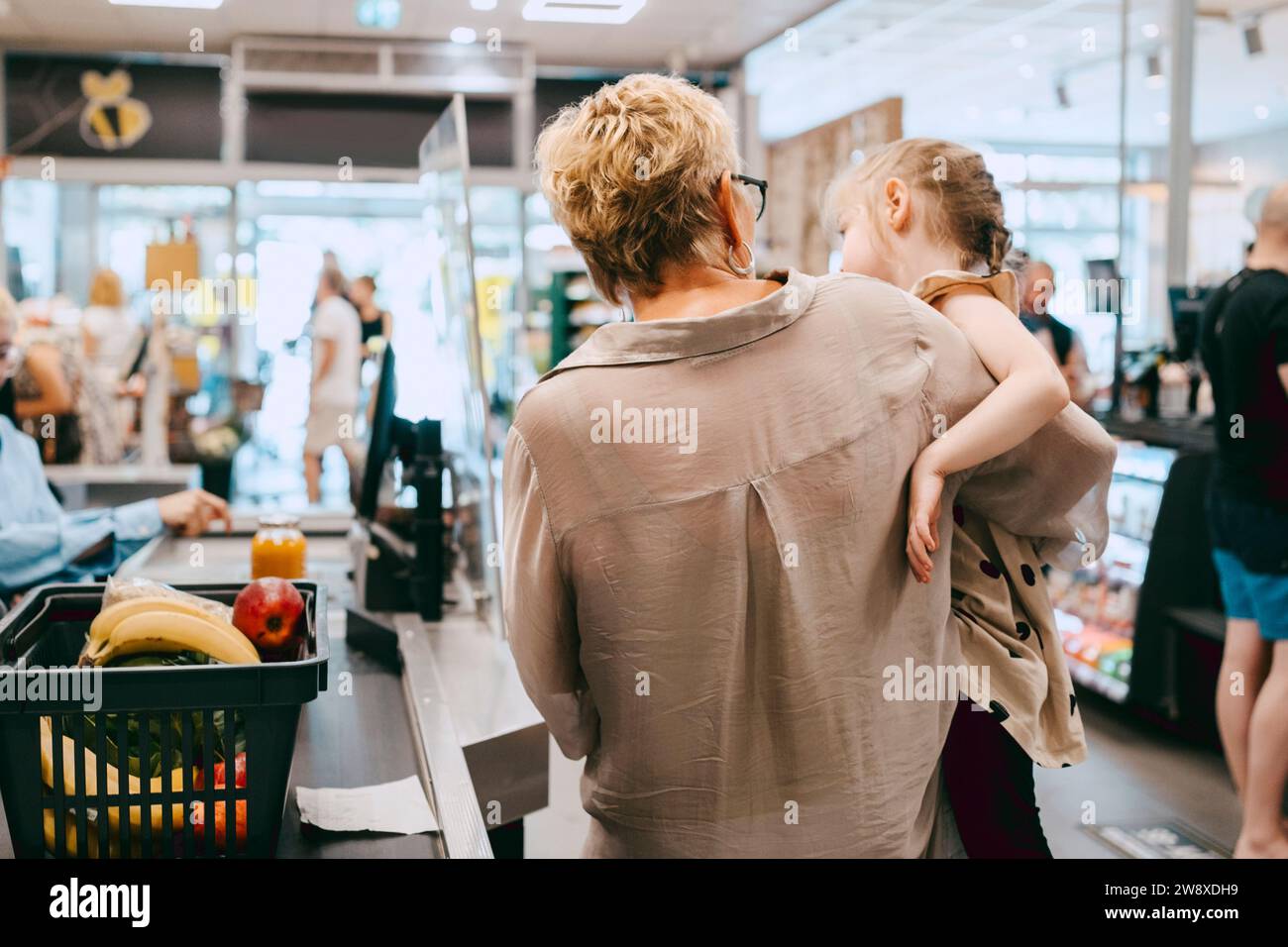 Grand-mère portant sa petite-fille tout en se tenant à la caisse dans le supermarché Banque D'Images