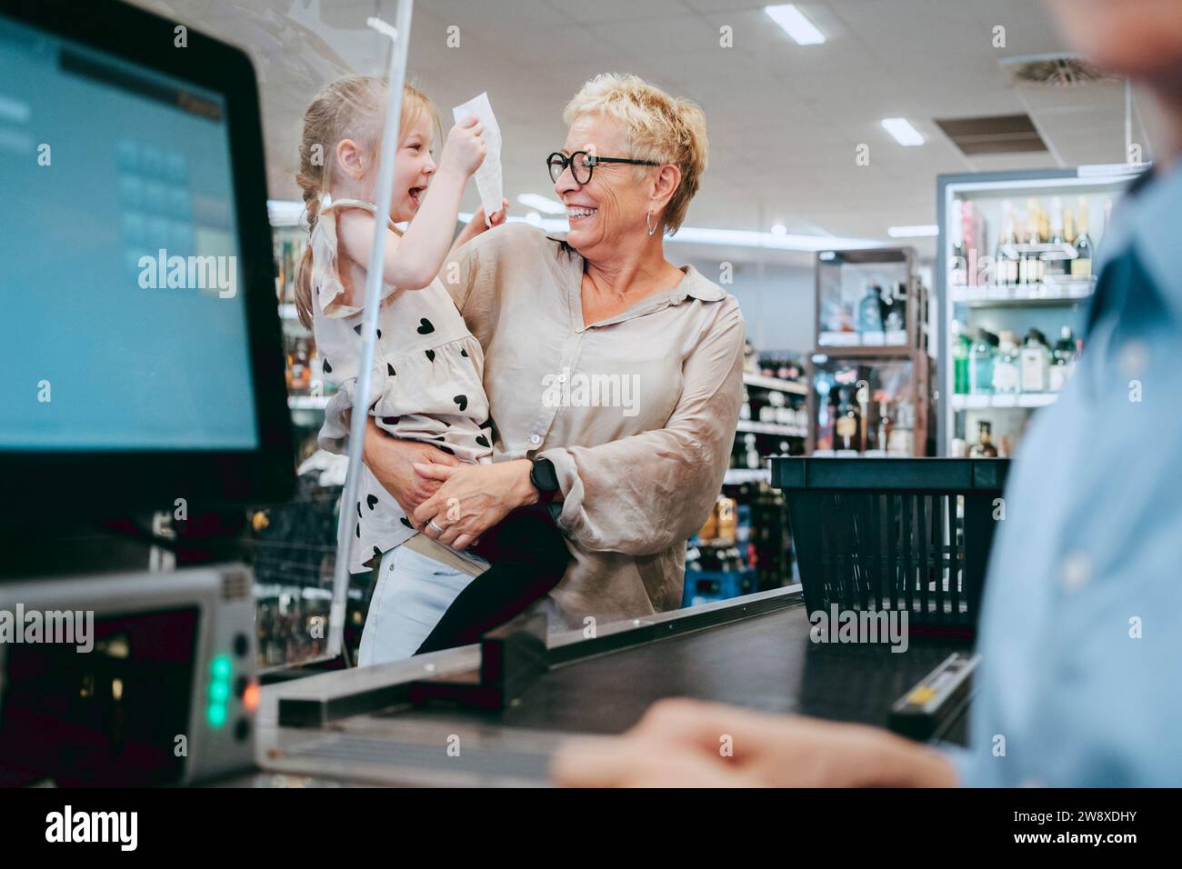 Heureuse femme âgée portant petite-fille joyeuse tenant la facture au supermarché Banque D'Images