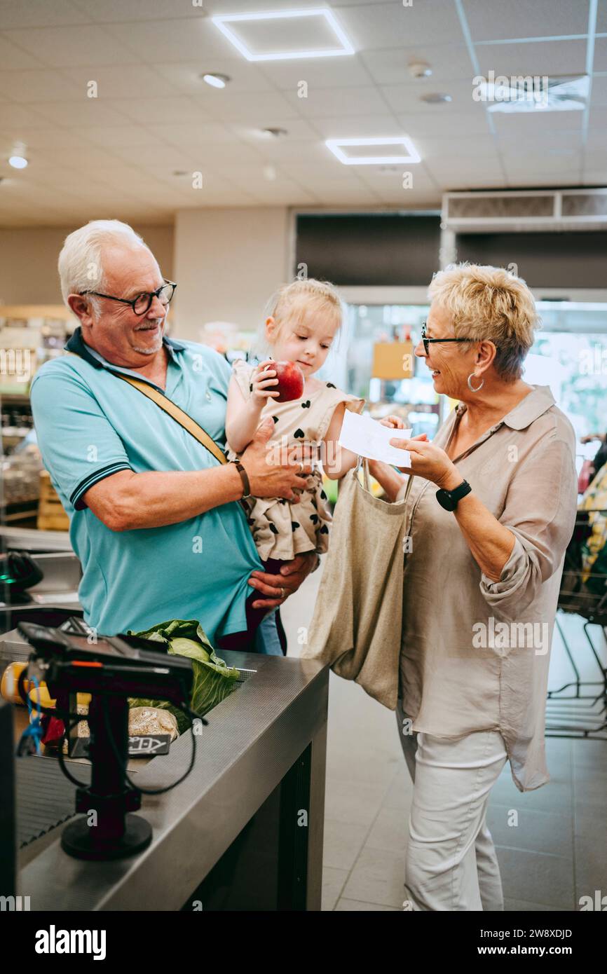 Fille aidant les grands-parents debout près du comptoir de caisse dans le supermarché Banque D'Images