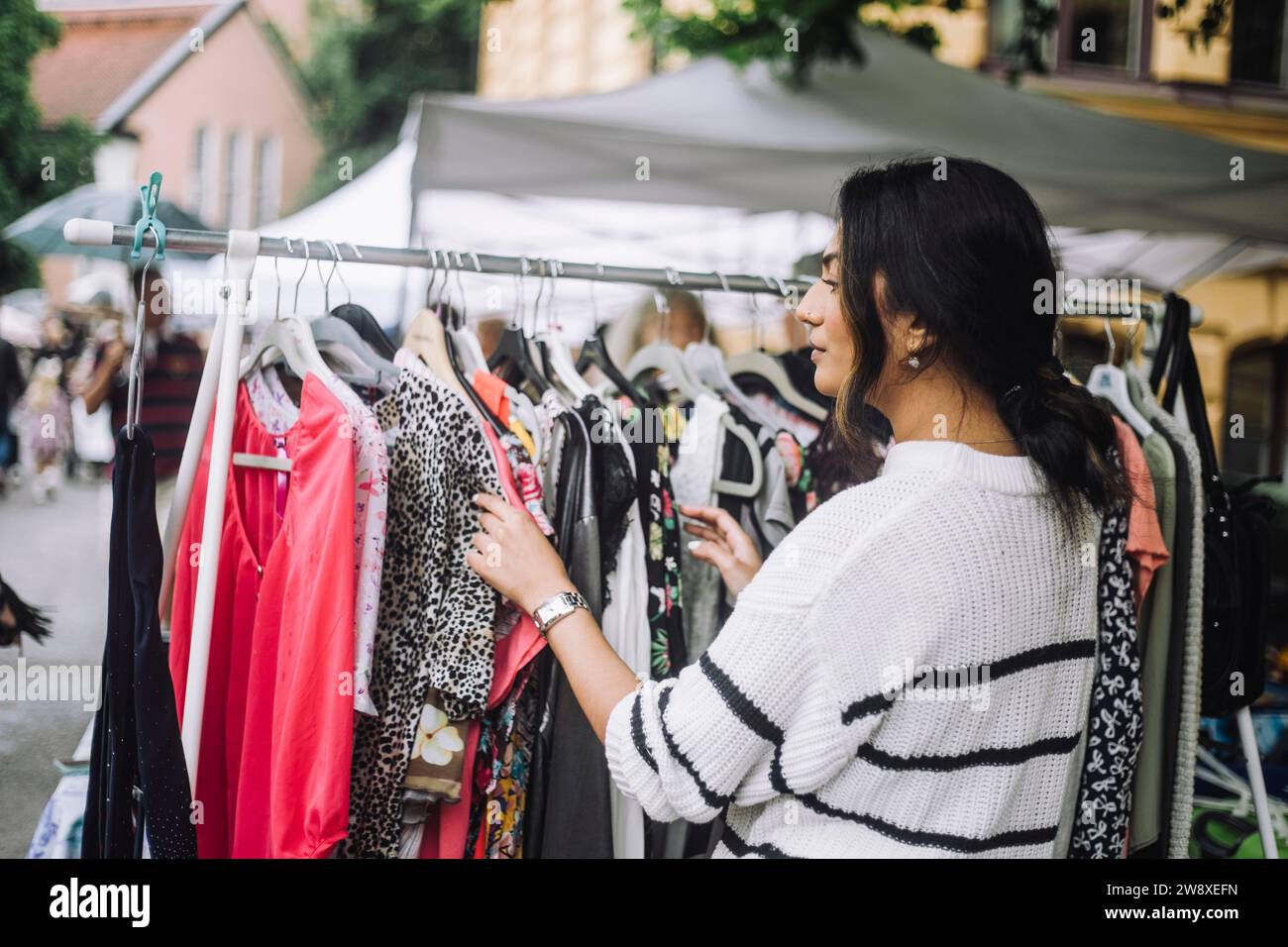 Jeune femme choisissant robe accrochée sur le porte-vêtements au marché aux puces Banque D'Images