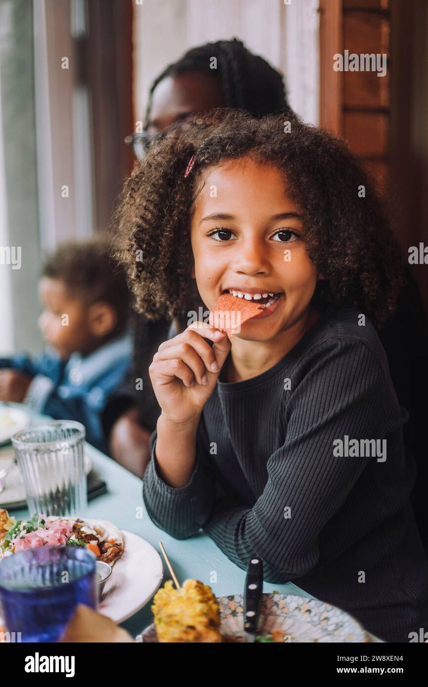 Portrait de fille souriante mangeant nacho chip assis au restaurant Banque D'Images