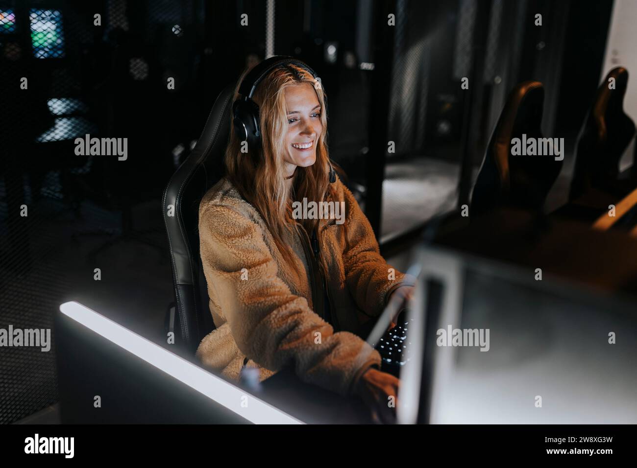 Femme souriante jouant au jeu vidéo dans le centre de jeu illuminé Banque D'Images