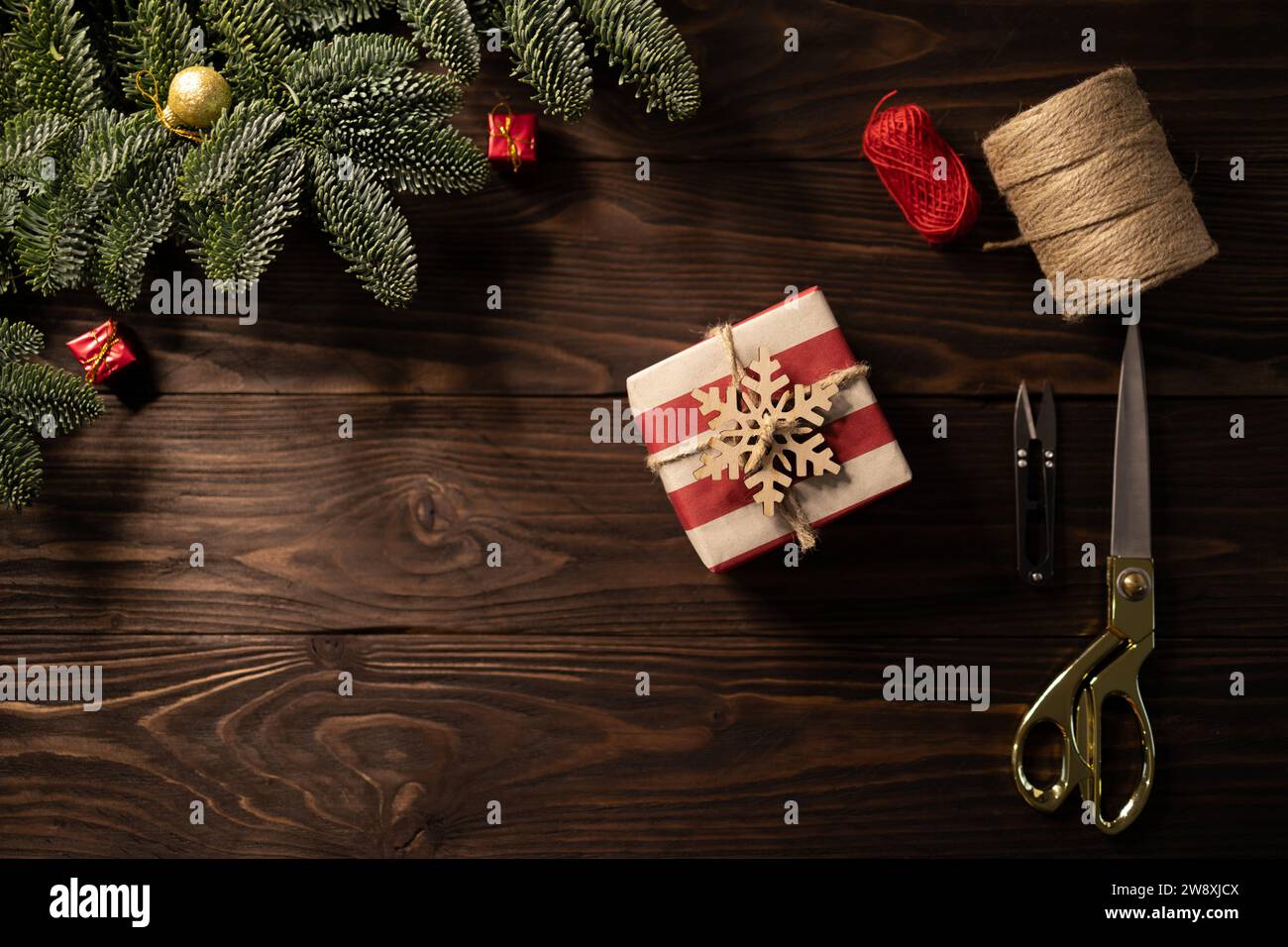 Vue de dessus du cadeau de Noël enveloppé dans du papier artisanal rayé et décoré de flocon de neige en bois sur fond en bois encadré par des branches de sapin noble Banque D'Images