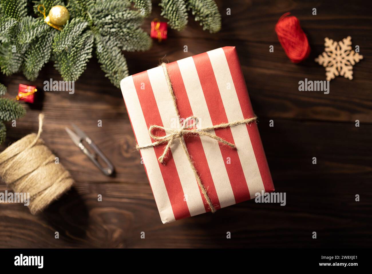 Gros plan de cadeau de Noël enveloppé dans du papier artisanal rayé et lacé avec cordon de toile de jute sur fond en bois Banque D'Images