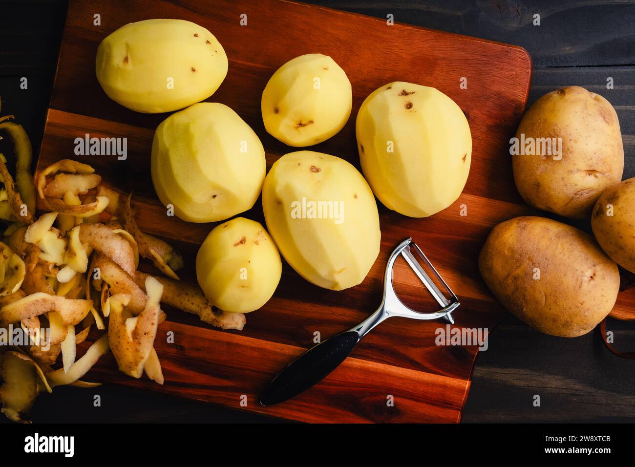 Pommes de terre Yukon Gold pelées sur une planche à découper en bois : pommes de terre jaune doré pelées et non pelées avec un éplucheur de légumes sur une table en bois Banque D'Images