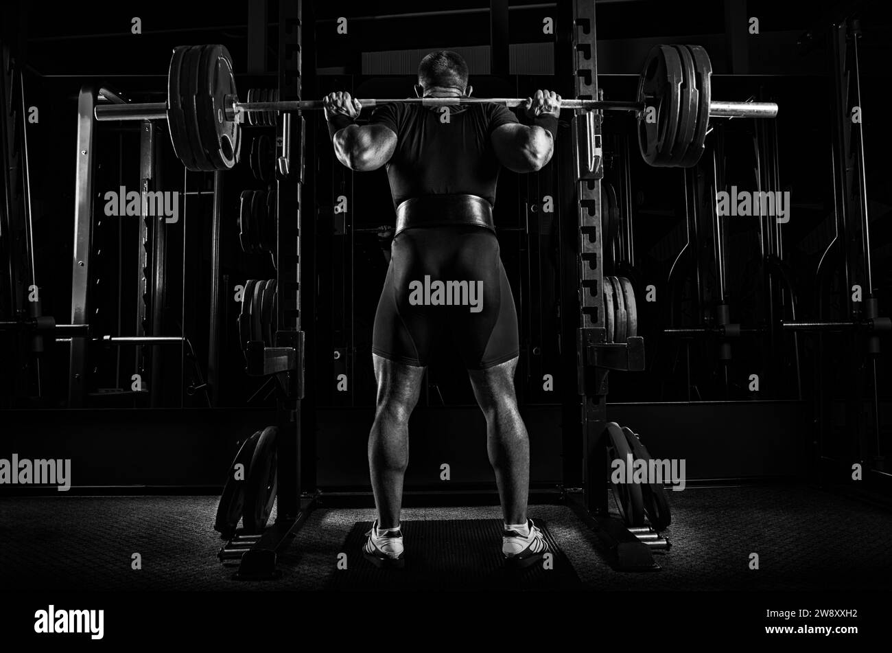 Athlète professionnel est debout avec une barre sur ses épaules et est sur le point de s'asseoir avec elle. Vue de l'arrière Banque D'Images